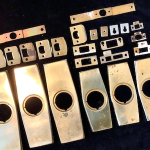 May include: Assortment of gold-toned metal door hardware pieces, including plates, knobs, and keyhole covers.