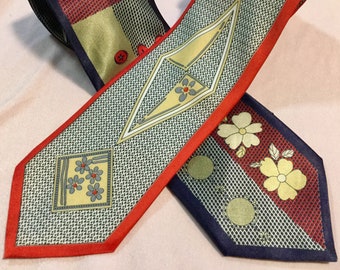May include: Two patterned neckties. One tie has a red border with a geometric design and a square with flowers. The other tie has a red border with a floral design and a navy blue background. Both ties have a textured background.