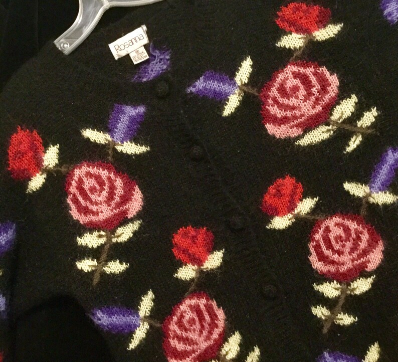 May include: Black knitted cardigan with a floral pattern featuring pink, red, and purple roses. The cardigan has a button closure and the label "Rosanna" is visible on the front.