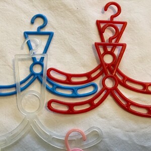 May include: A set of three plastic hangers in red, blue, and clear. The hangers are designed for hanging clothes and have a unique shape with multiple loops.