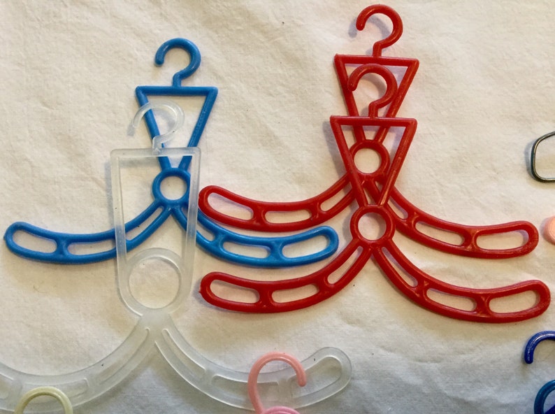 May include: A set of three plastic hangers in red, blue, and clear. The hangers are designed for hanging clothes and have a unique shape with multiple loops.