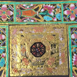 May include: A square, gold-colored frame with a black and white octagon in the center. The frame is decorated with floral designs in pink, blue, and green.