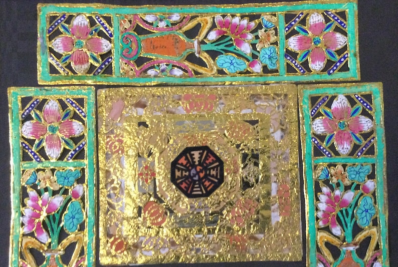 May include: A square, gold-colored frame with a black and white octagon in the center. The frame is decorated with floral designs in pink, blue, and green.