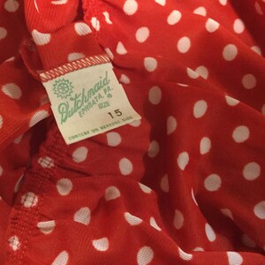 May include: Red fabric with white polka dots and a white tag that says "Dutchmaid Ephrata, PA. Size 15 Content on Reverse Side"