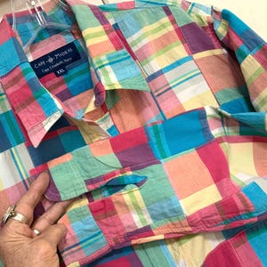 May include: A colorful, patchwork-style button-down shirt in a variety of colors including pink, blue, green, and yellow. The shirt has a collar and a pocket. The label reads "CAPE MADRAS Cape Elizabeth, Maine XXL".