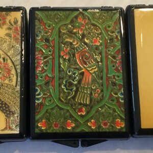 May include: Three decorative compact cases with black frames. The first features two peacocks and floral designs in gold, red, and green. The second has a bird and floral design in green and red. The third has a hummingbird and floral design.