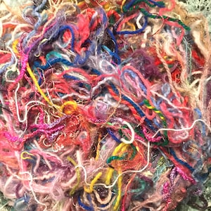 May include: A close-up of a pile of colorful yarn scraps in various shades of pink, purple, blue, green, yellow, and red. The yarn is tangled and messy, creating a textured and abstract image.