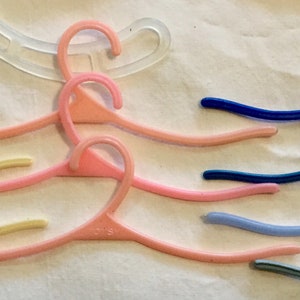 May include: A collection of colorful plastic hangers, some with the word "Totsey" printed on them. The hangers are arranged in a wave-like pattern on a white surface.