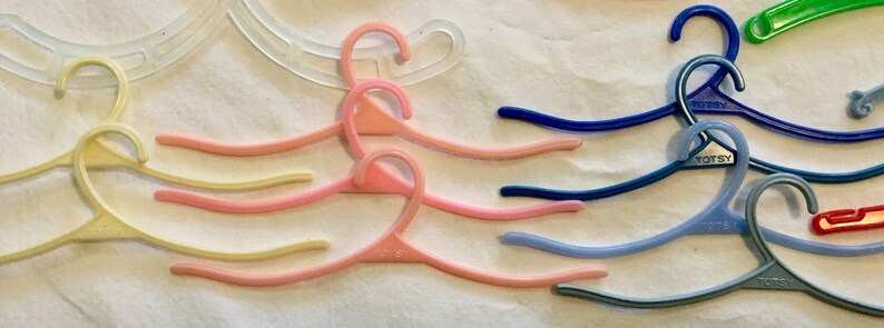 May include: A collection of colorful plastic hangers, some with the word "Totsey" printed on them. The hangers are arranged in a wave-like pattern on a white surface.