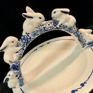 May include: A white ceramic serving dish with a blue and white floral design. The dish is shaped like a ring with four rabbit figurines attached to the ring. The rabbits are painted in a blue and white pattern.