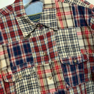 May include: A patchwork plaid shirt in red, navy, cream, and tan. The shirt has two button-flap chest pockets and a button-down collar. The shirt is made of a soft, woven fabric and features a classic, casual style.