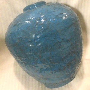 May include: A blue ceramic vase with a textured surface. The vase has a rounded shape and a wide opening.