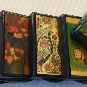 May include: A series of connected, rectangular boxes with hinged sides. Each box features a different design, including floral patterns, a peacock, and a sheep. The boxes are black with colorful, detailed artwork.