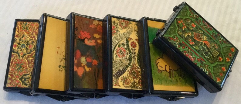 May include: A series of connected, rectangular boxes with hinged sides. Each box features a different design, including floral patterns, a peacock, and a sheep. The boxes are black with colorful, detailed artwork.