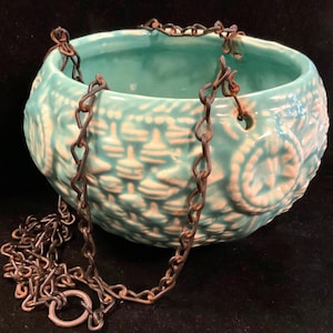 May include: A turquoise ceramic hanging planter with a white embossed design and a rusty metal chain.