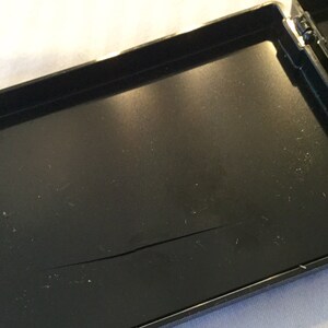 May include: An open, black, rectangular case with a hinged lid. The interior of the case is black and has a crack running across the bottom. The case is on a white surface.