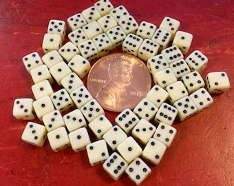 May include: A large group of white dice with black dots, scattered on a red surface. A US penny coin is in the center of the dice.