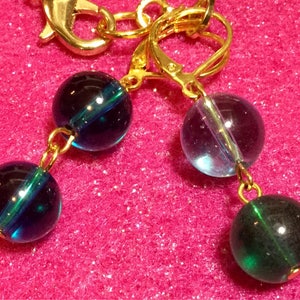 May include: A pair of earrings with gold hoops and three glass beads. The beads are dark blue with a green stripe, light blue with a green stripe, and dark green.