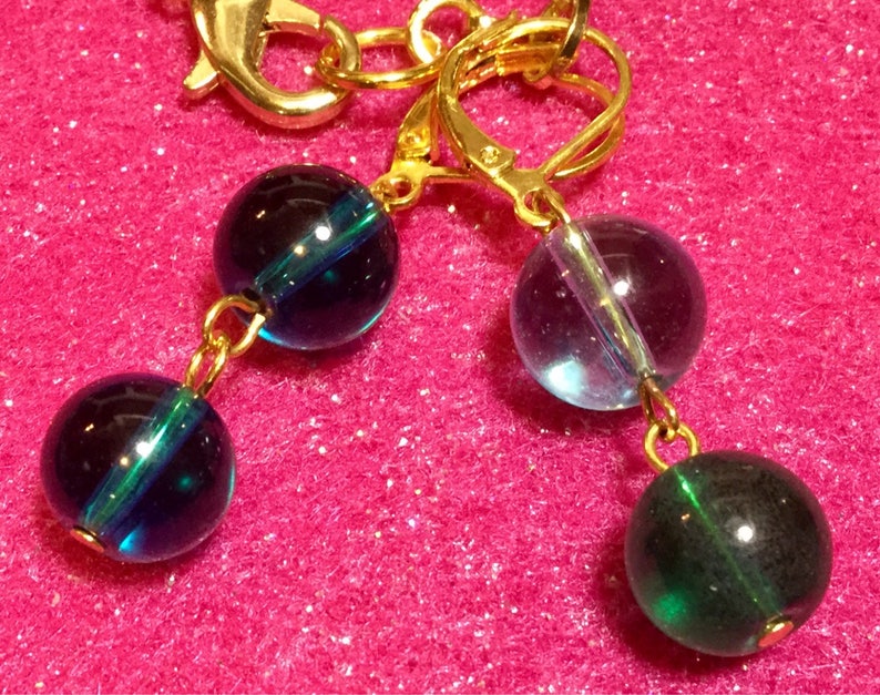 May include: A pair of earrings with gold hoops and three glass beads. The beads are dark blue with a green stripe, light blue with a green stripe, and dark green.