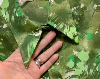 May include: A green button-up shirt with a vibrant, abstract pattern in shades of green and white. The shirt features a classic collar and button closure. The fabric has a soft, flowing appearance, suggesting a comfortable fit.