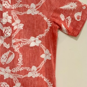 May include: A red short-sleeved button-down shirt with a white floral print. The shirt has a pocket on the left side and the text "Reyn Spooner" on the tag.