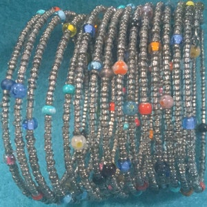 May include: A stack of silver beaded bracelets with colorful glass beads. The bracelets are stacked on top of each other, creating a colorful and textured look.