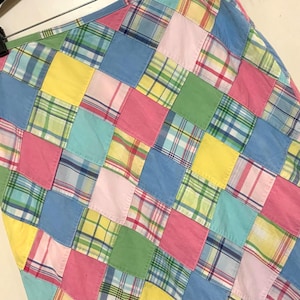 May include: A colorful patchwork skirt featuring a variety of plaid and solid squares in shades of pink, blue, green, and yellow. The skirt is hanging on a hanger, showcasing its design and construction.