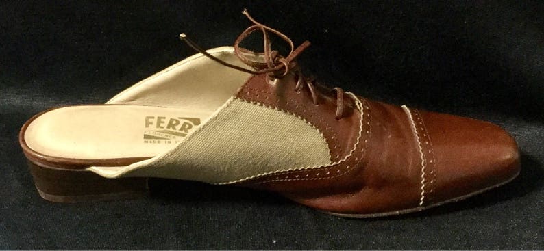 May include: Brown leather slip-on shoe with a beige canvas panel and white stitching. The shoe has a lace-up design and the brand name "FERR" is visible on the insole.