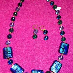 May include: A gold chain necklace with blue and green glass beads and rectangular glass pendants. Matching earrings with blue and green glass beads are included.