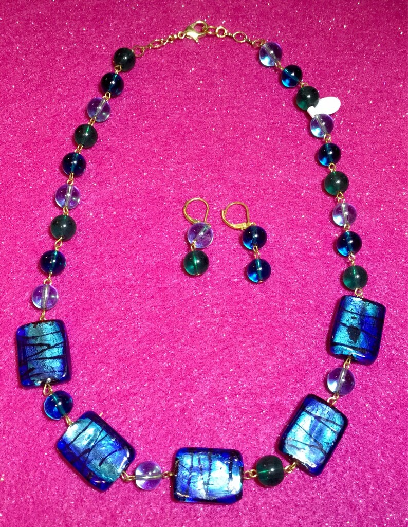 May include: A gold chain necklace with blue and green glass beads and rectangular glass pendants. Matching earrings with blue and green glass beads are included.