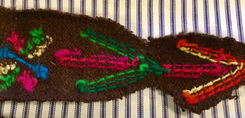 K&ouml;nnte beinhalten: Ein brauner Stoffstreifen mit bunter Stickerei. Die Stickerei zeigt eine Vielzahl von Farben, darunter Gr&uuml;n, Pink, Blau, Orange und Gelb. Die Stickerei hat die Form von Blumen und Bl&auml;ttern.