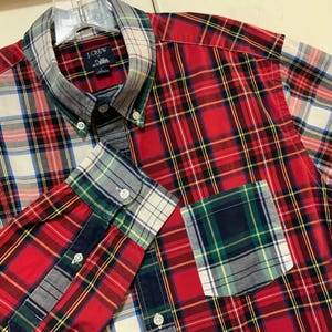 May include: A button-down plaid shirt with a mix of red, white, green, and blue patterns. The shirt features a button-down collar, a chest pocket, and the J.Crew label.