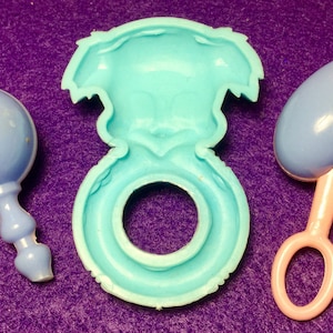 Pode incluir: Tr&ecirc;s brinquedos de beb&eacute; de pl&aacute;stico azul. Um &eacute; um chocalho em forma de bola, outro &eacute; um anel e o terceiro &eacute; um chocalho em forma de cora&ccedil;&atilde;o.
