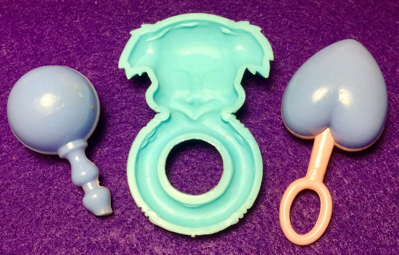 Pode incluir: Tr&ecirc;s brinquedos de beb&eacute; de pl&aacute;stico azul. Um &eacute; um chocalho em forma de bola, outro &eacute; um anel e o terceiro &eacute; um chocalho em forma de cora&ccedil;&atilde;o.