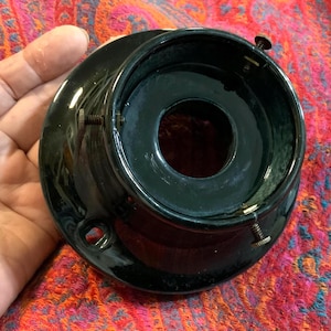 May include: A glossy black ceramic lamp shade fitter featuring a circular base with a central opening and three evenly spaced metal thumb screws around the rim for securing a glass shade. The component has a smooth, reflective finish.