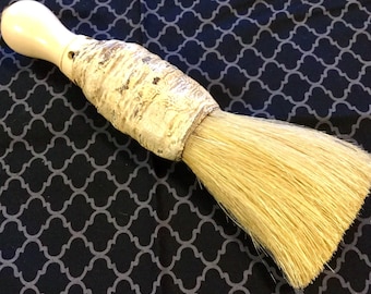 May include: A brush with a white handle and a long, natural bristle head. The handle is made of a textured material and has a hole in the side.