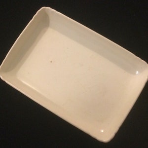 May include: A white ceramic rectangular serving tray with slightly scalloped edges. The tray has a smooth, glossy finish and shows signs of light wear.