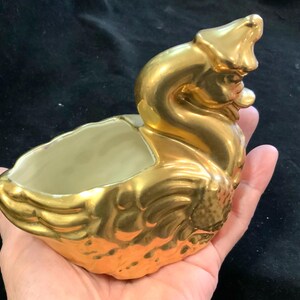 May include: A gold ceramic swan planter with a white interior. The swan has a detailed design and is a vintage style.
