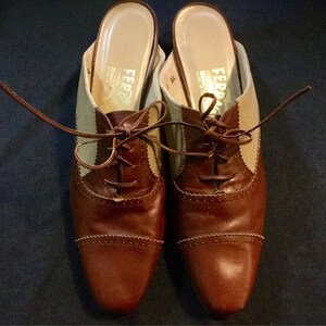 May include: A pair of brown leather shoes with beige canvas panels and laces. The shoes have a rounded toe and a low heel.