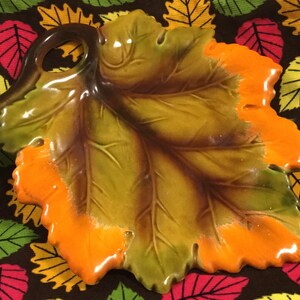 May include: A ceramic leaf-shaped dish with a brown, green, and orange glaze. The dish has a raised edge and a hole in the center.