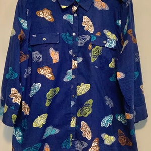 May include: A navy blue button-down shirt with a butterfly pattern. The long-sleeved shirt features a classic collar, two chest pockets, and a button-up front. The butterflies are in shades of white, brown, green, and blue.