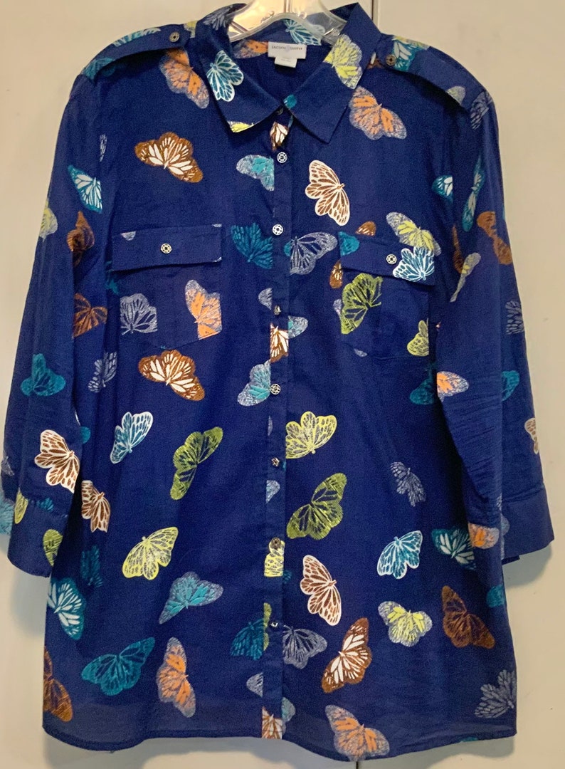 May include: A navy blue button-down shirt with a butterfly pattern. The long-sleeved shirt features a classic collar, two chest pockets, and a button-up front. The butterflies are in shades of white, brown, green, and blue.