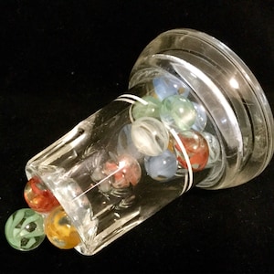 May include: A clear glass jar with a white band around the top, filled with colorful marbles. The marbles are red, blue, green, and white.