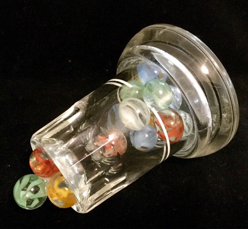 May include: A clear glass jar with a white band around the top, filled with colorful marbles. The marbles are red, blue, green, and white.