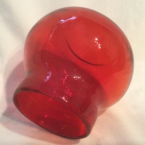 May include: A red glass lampshade with a round, bulbous shape and a smooth, shiny surface.