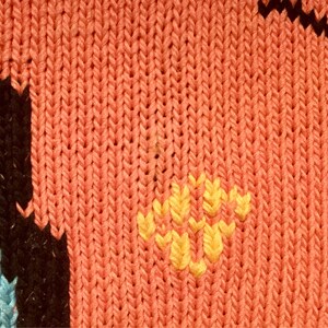 K&ouml;nnte beinhalten: Nahaufnahme eines gestrickten Stoffes mit rotem Hintergrund und gelbem Blumendesign.