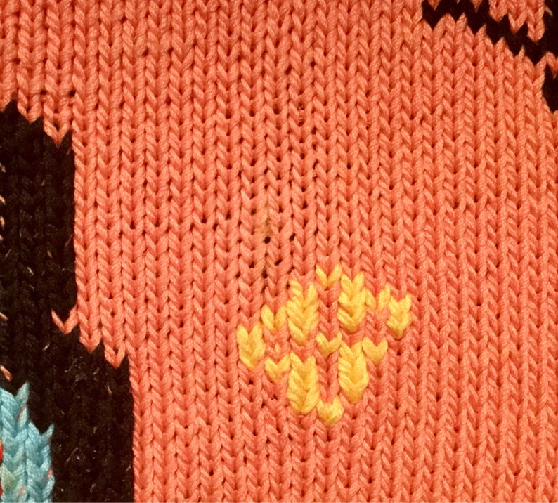 K&ouml;nnte beinhalten: Nahaufnahme eines gestrickten Stoffes mit rotem Hintergrund und gelbem Blumendesign.