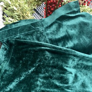 May include: A deep green velvet fabric with a soft, plush texture. The fabric is folded and draped, showcasing its rich color and luxurious feel.