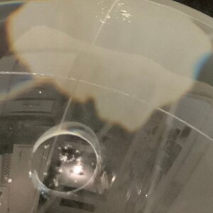 Op de afbeelding: Een close-up van een heldere glazen bol met een witte, bewolkte binnenkant. De bol is licht vervormd, waardoor een rippelend effect ontstaat. De bol ligt op een donker oppervlak.
