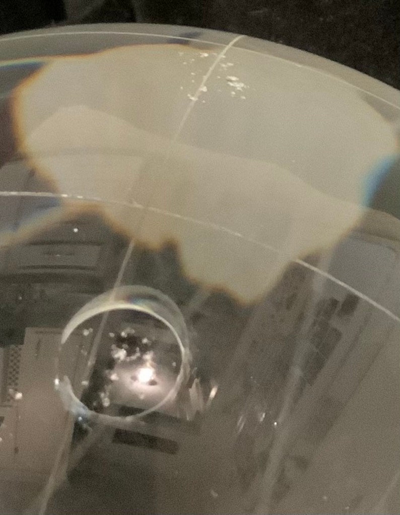 Op de afbeelding: Een close-up van een heldere glazen bol met een witte, bewolkte binnenkant. De bol is licht vervormd, waardoor een rippelend effect ontstaat. De bol ligt op een donker oppervlak.